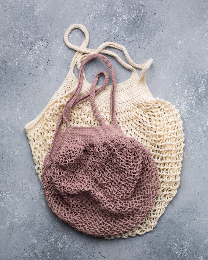 Two knitted reusable mesh bags in beige and pink, ideal for eco-friendly shopping.