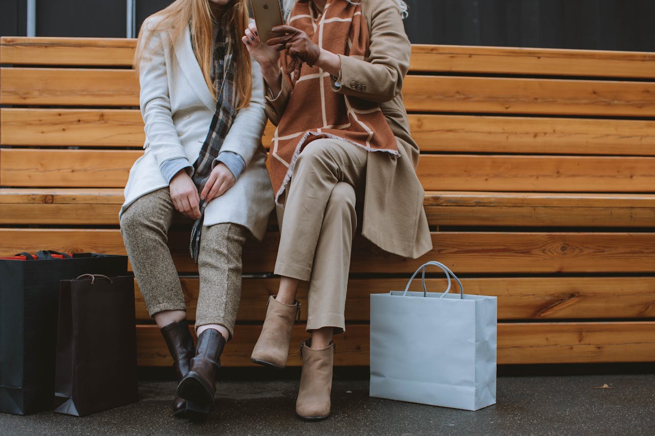 Two stylish women seated on a bench with shopping bags, capturing a fashionable urban vibe.